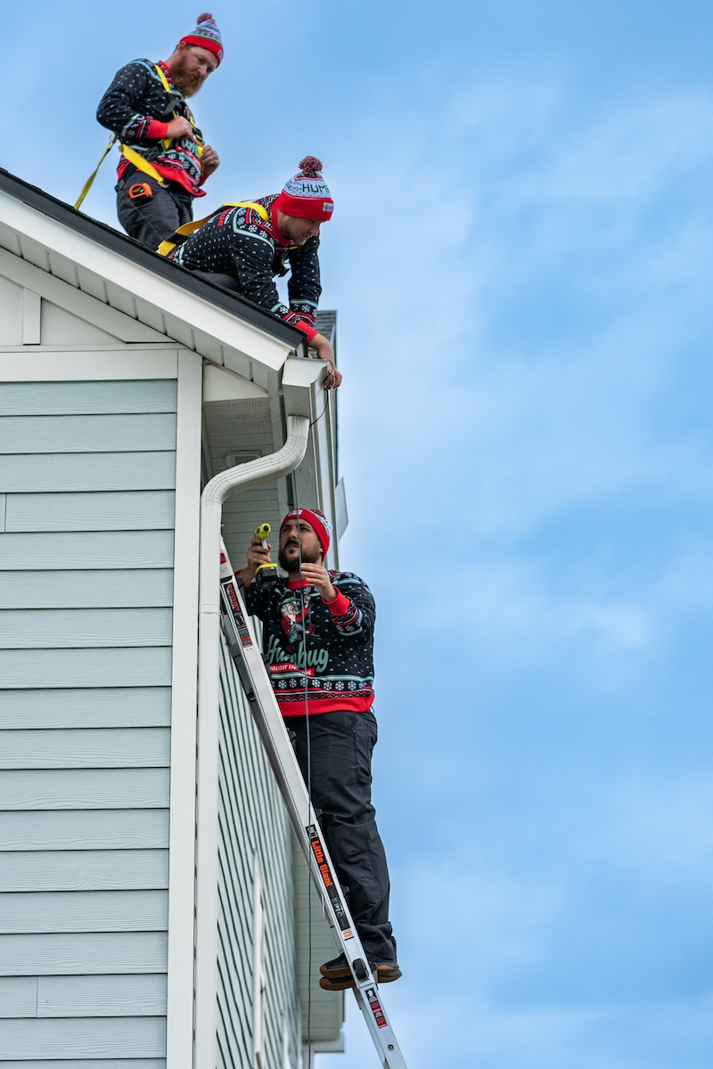 Humbug Holiday Lighting crew installs outdoor Christmas lights along the roofline and gutters of a home.