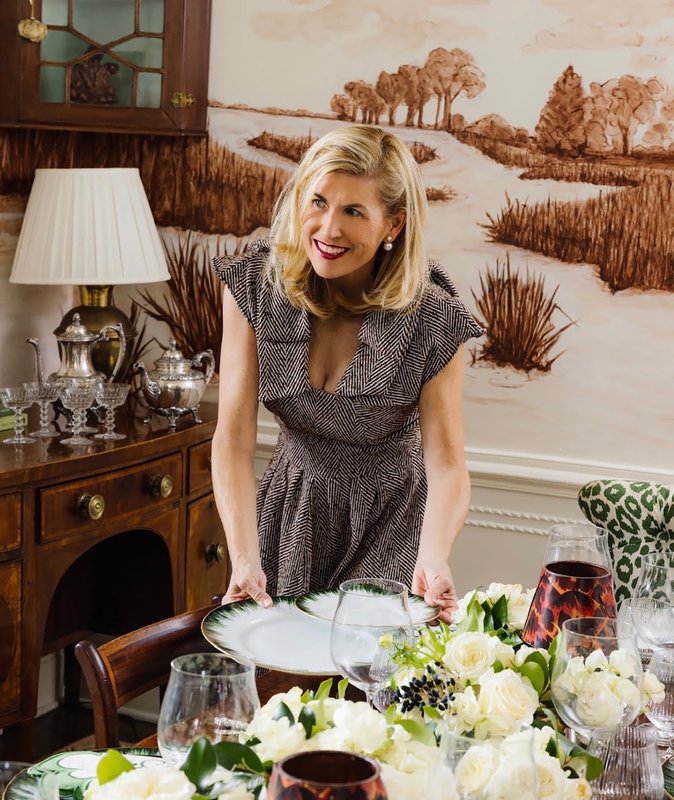 Leslie May leaning over a dining table decorated with white flowers, patterned plates and glassware