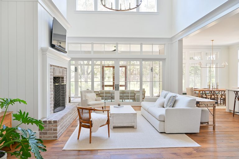 Bright Spring Island living room with white sofa, brick fireplace, tall windows and warm wood floors