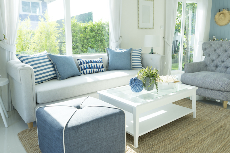 Bright living room with white sofa, blue cushions, upholstered chair and large windows
