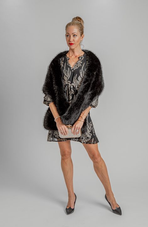 Christina Mulshenock wearing a patterned black dress, dark wrap, pointed heels and a metallic clutch