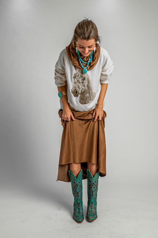 Martha Powell wearing a horse-print sweater over a bronze dress with turquoise Western boots and statement jewelry.