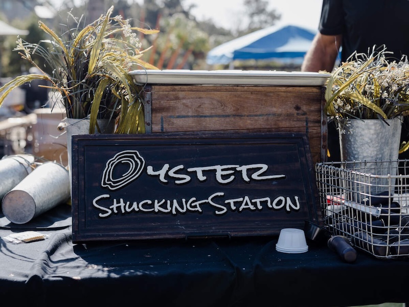 Oyster shucking station sign displayed at an outdoor seafood festival.