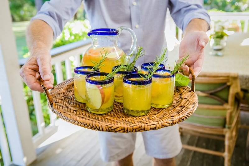Tray of yellow fruit-filled cocktails garnished with rosemary