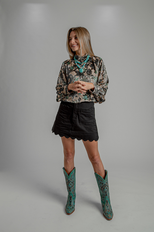 Woman wearing a floral top, black scalloped skirt, turquoise jewelry and turquoise Western boots.