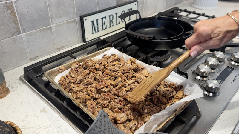 Candied pecans on a parchment-lined baking tray being stirred with a wooden utensil.
