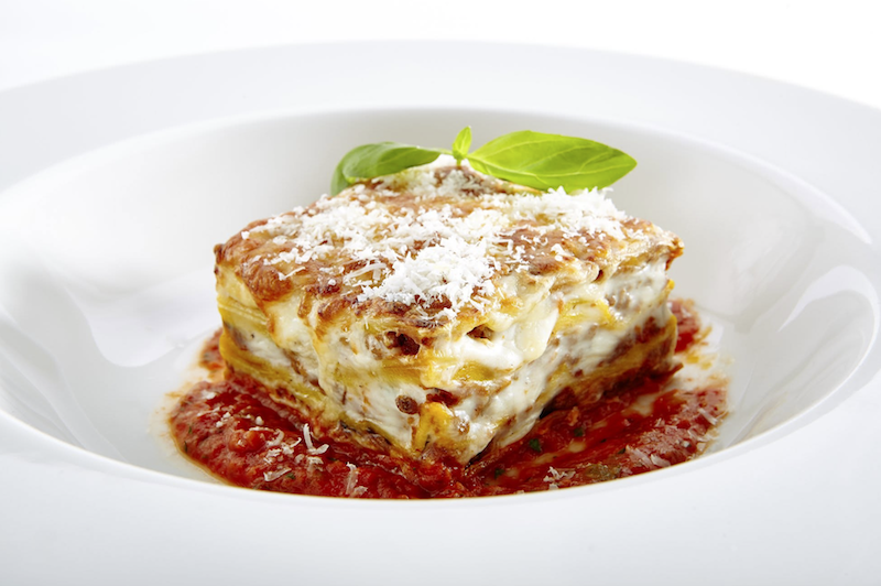 Square serving of baked lasagna topped with melted cheese and tomato sauce.