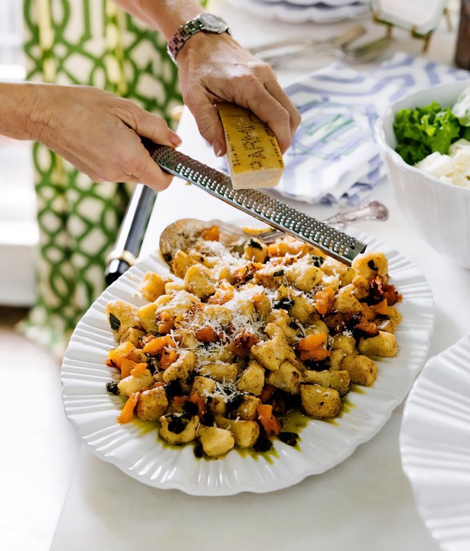 Hands serving a colorful prepared dish from a white platter onto a dining table