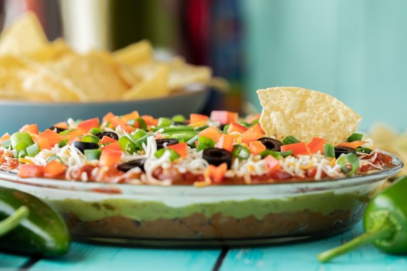 Layered party dip topped with chopped vegetables, cheese and tortilla chips.