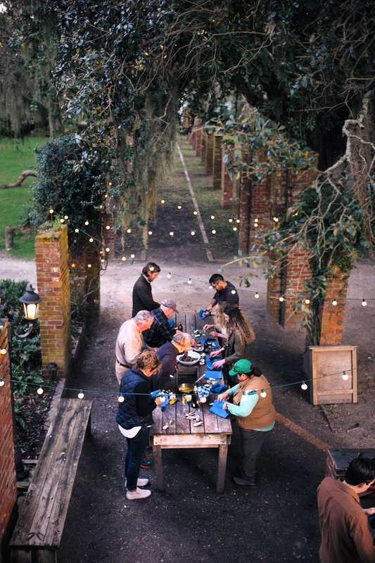 Guests sharing an oyster roast beneath trees and string lights