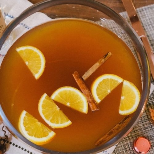 Bowl of autumn punch with floating orange and apple slices surrounded by seasonal ingredients.