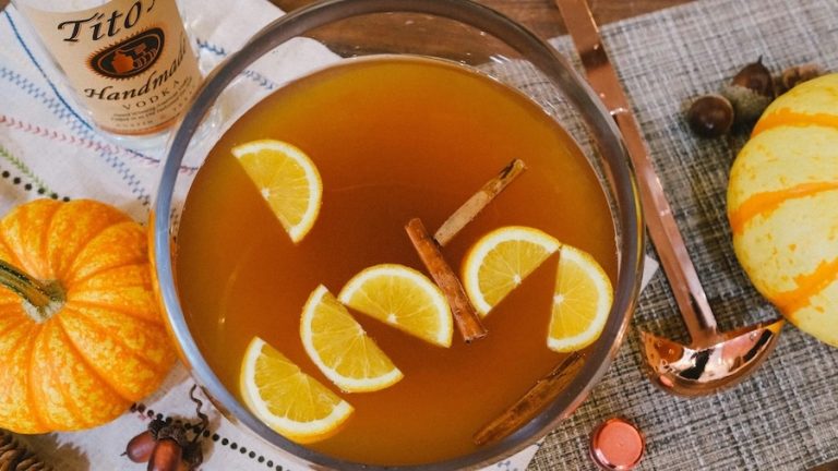 Bowl of autumn punch with floating orange and apple slices surrounded by seasonal ingredients.