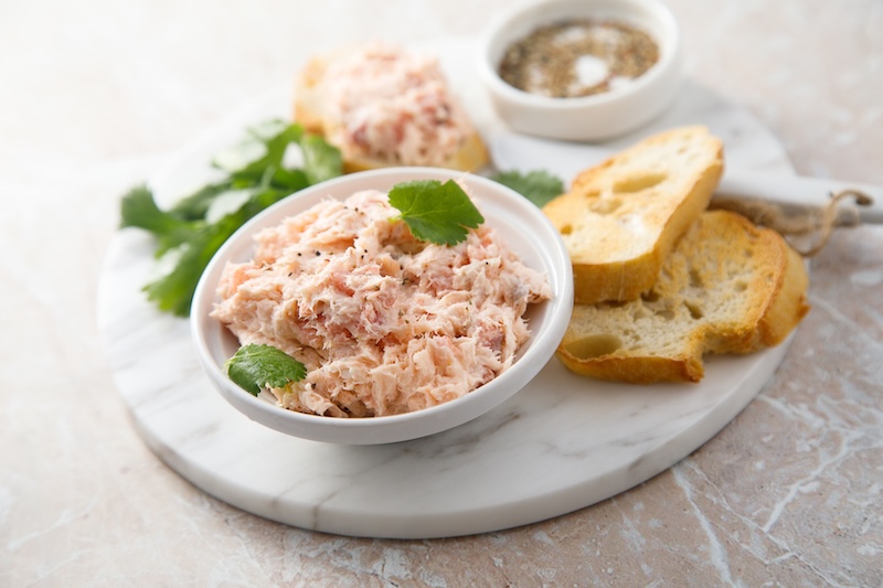 Smoked salmon dip served in a white bowl with crostini and lemon.