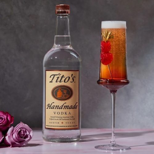 Tito’s vodka bottle beside a tall sparkling berry cocktail garnished with a raspberry and rosemary.